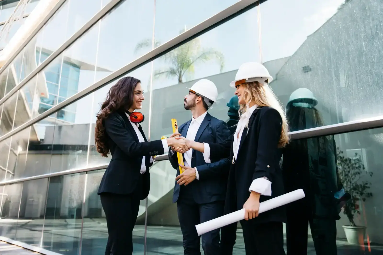 A woman and two men in hard hats shaking hands at a construction site.