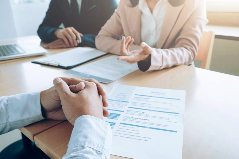 Job interview in progress — candidate sitting across from two interviewers with a resume on the table.